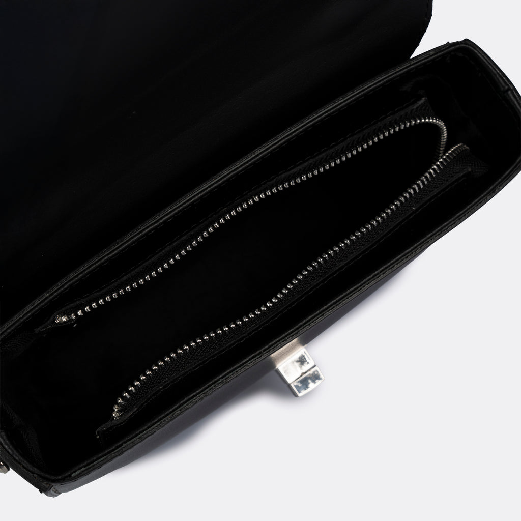 Compact black top-handle bag in Pelle Ruga leather with silver-tone turn-lock bar, the Capri
